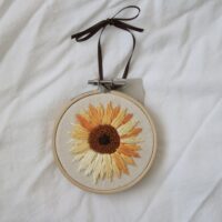 Hand embroidered sunflower framed in a wooden hoop and tied with a brown ribbon