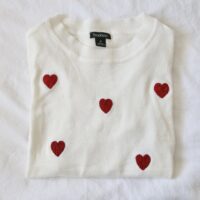 A white jumper folded up and hand embroidered with love hearts