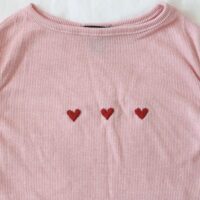 A close up of three hand embroidered hearts on a pink and white top