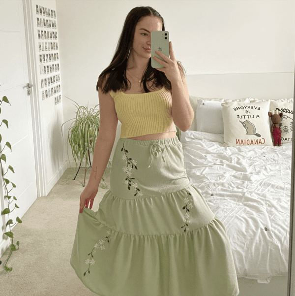 brunette girl wearing a sage green maxi skirt hand embroidered with daisies and vines trailing down