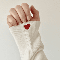 the sleeve of a white jumper and a red heart hand embroidered on the sleeve cuff