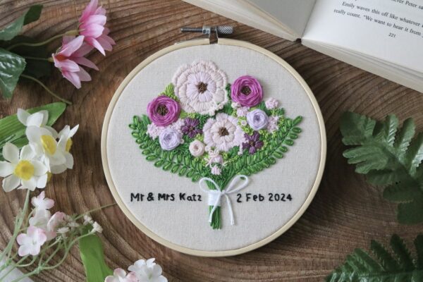 A 6 inch hoop hand embroidered with a purple bouquet of flowers and text reading "Mr & Mrs Katz. 2 Feb 2024"