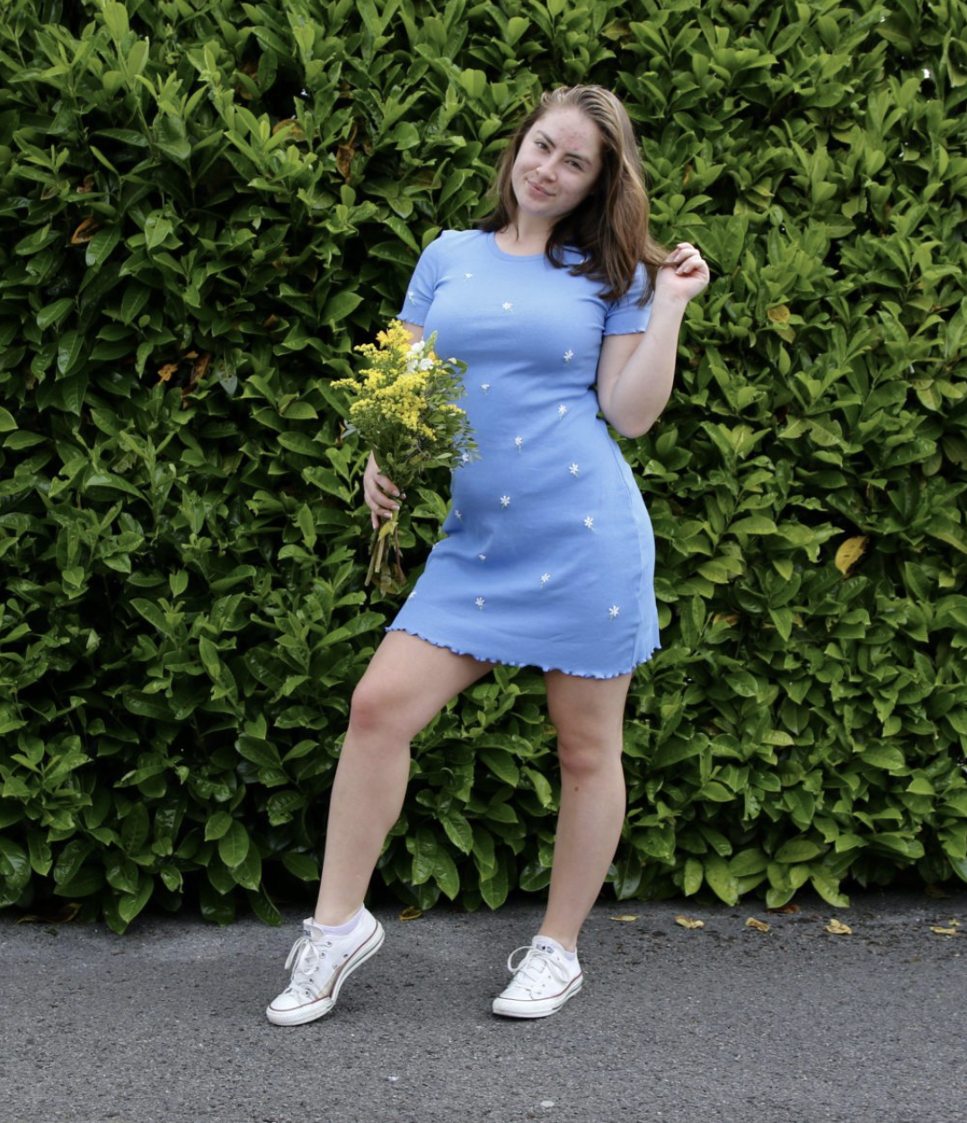 a brunette girl holding a yellow bouquet wearing a blue body con dress hand embroidered with daisies