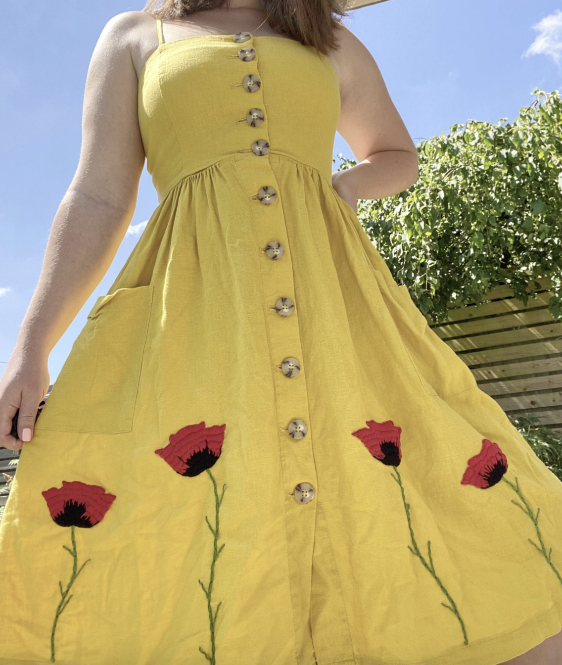 A yellow dress hand embroidered with red stem poppies growing from the bottom of the skirt