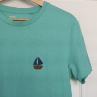 A turquoise blue tee hand embroidered with a navy blue sail boat on the left breast