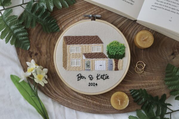 a 6 inch hoop hand embroidered with the front of a custom house with the names 'Ben & Katie' and the year '2024'