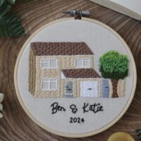 a 6 inch hoop hand embroidered with the front of a custom house with the names 'Ben & Katie' and the year '2024'