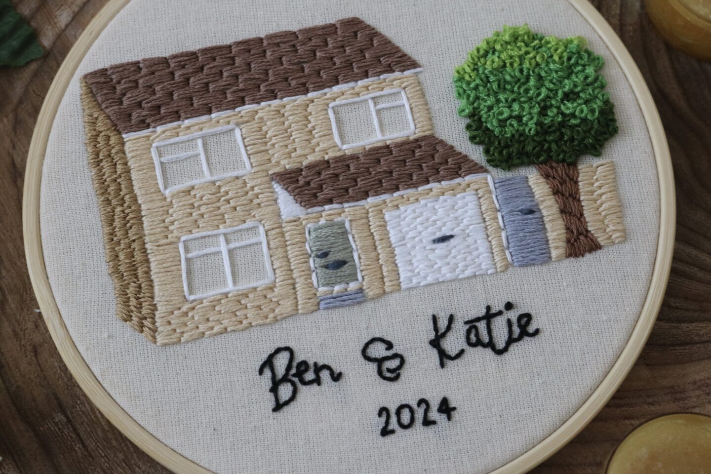Close up of a hand embroidered house with a tree and the text 'Ben & Katie 2024'