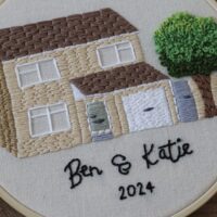 Close up of a hand embroidered house with a tree and the text 'Ben & Katie 2024'