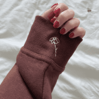 A cream embroidered flower on the cuff of a dark brown hoodie sleeve.