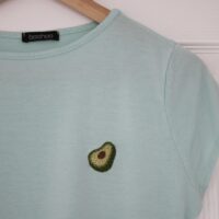 A close up of a mint blue t-shirt hand embroidered with an avocado slice