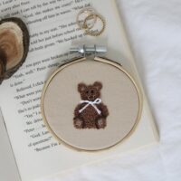 A 3 inch embroidery hoop hand embroidered with a teddy bear on a beige cotton fabric