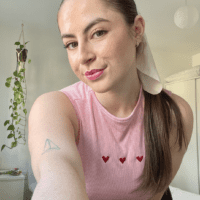 Brunette girl with her hair in a ponytail wearing a pink top hand embroidered with three red love hearts