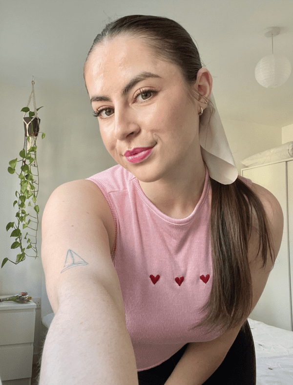 Brunette girl with her hair in a ponytail wearing a pink top hand embroidered with three red love hearts