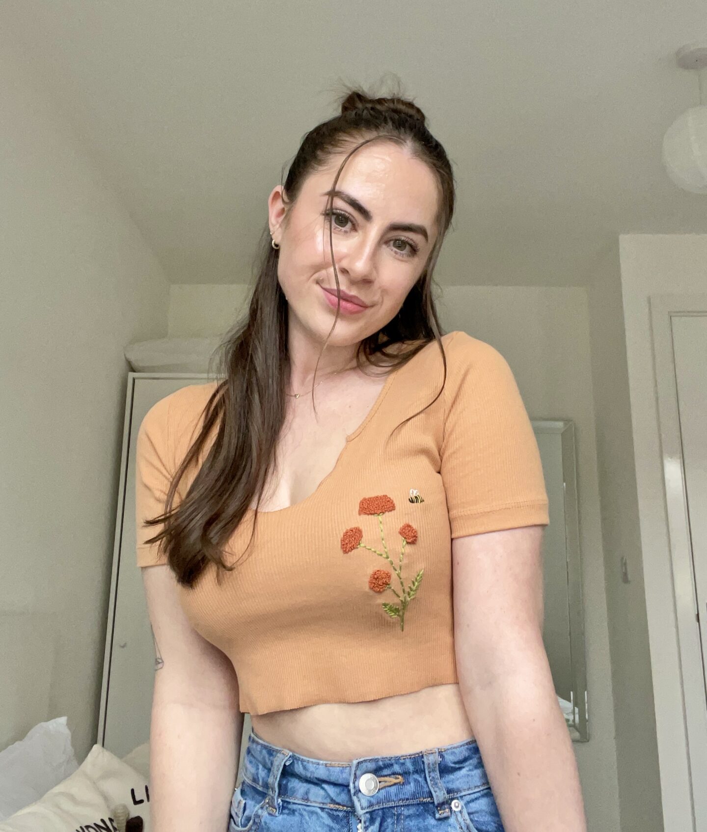 A brunette girl wearing a hand embroidered terracotta coloured top with a hydrangea flower and bee