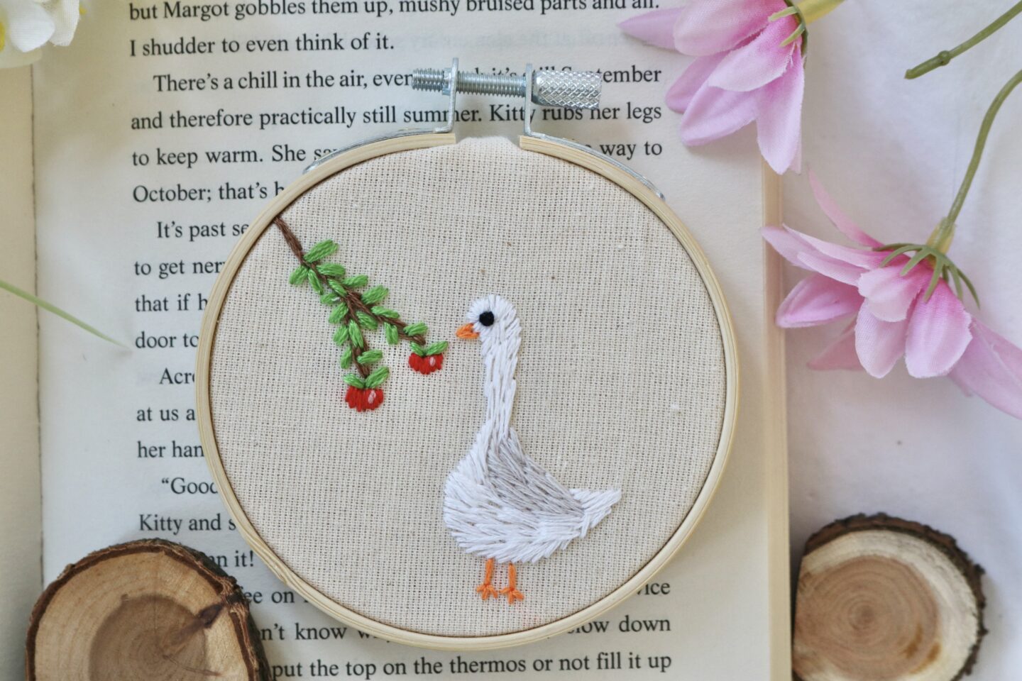 Hand-embroidered 3-inch hoop featuring a white goose standing next to a branch with red apples, stitched on natural cotton fabric and framed in a wooden embroidery hoop.