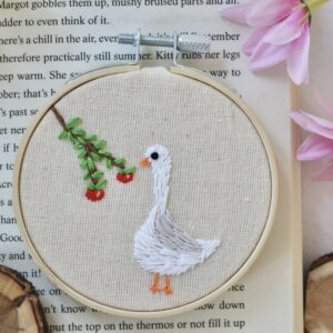 Hand-embroidered 3-inch hoop featuring a white goose standing next to a branch with red apples, stitched on natural cotton fabric and framed in a wooden embroidery hoop.