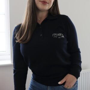 A brunette girl wearing a navy blue polo knit hand embroidered with an outline of the Canadian rockies