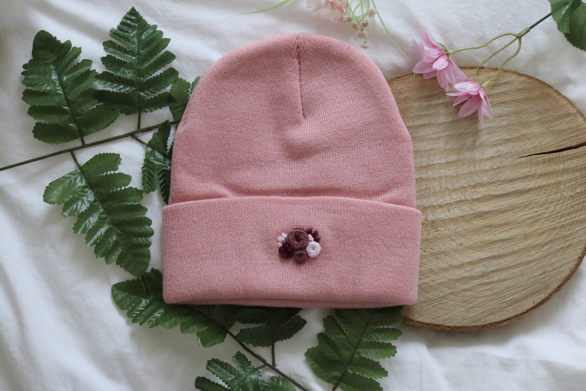 A pink knitted beanie hand embroidered with purple roses and cosmos flowers