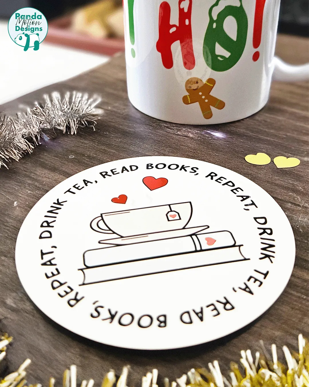 A white coaster with a black outline of a pile of books and a mug on top with the wording 'read books, drink tea, repeat'