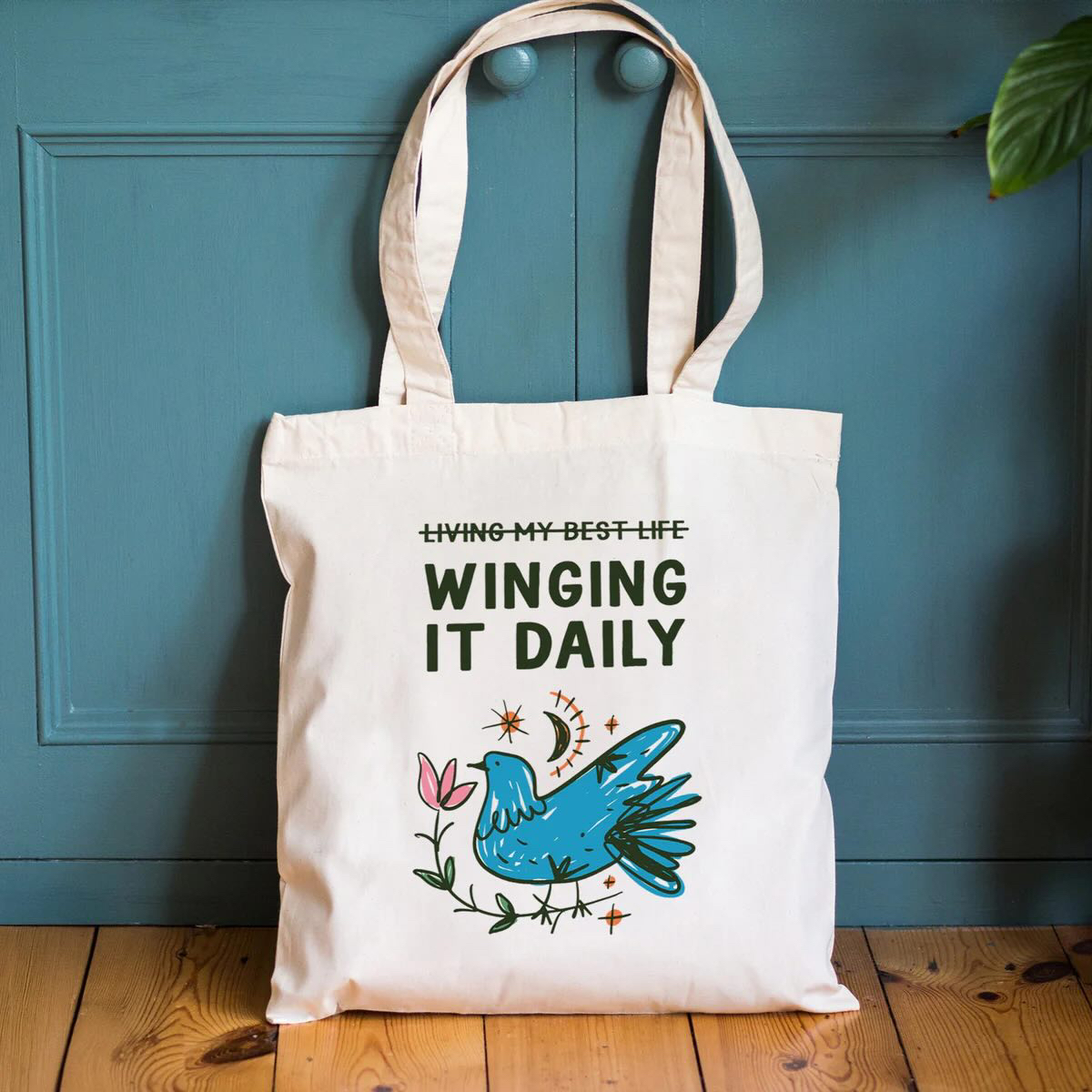 A tote bag with a bird and the wording 'living my best life' with a strikethrough and underneath the wording 'winging it daily'