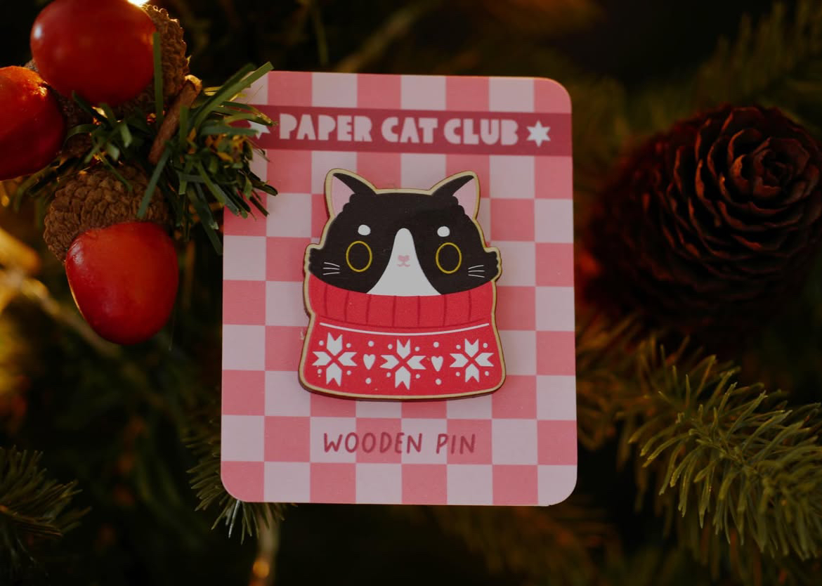 A pin of a black and white cat wearing a Christmas jumper