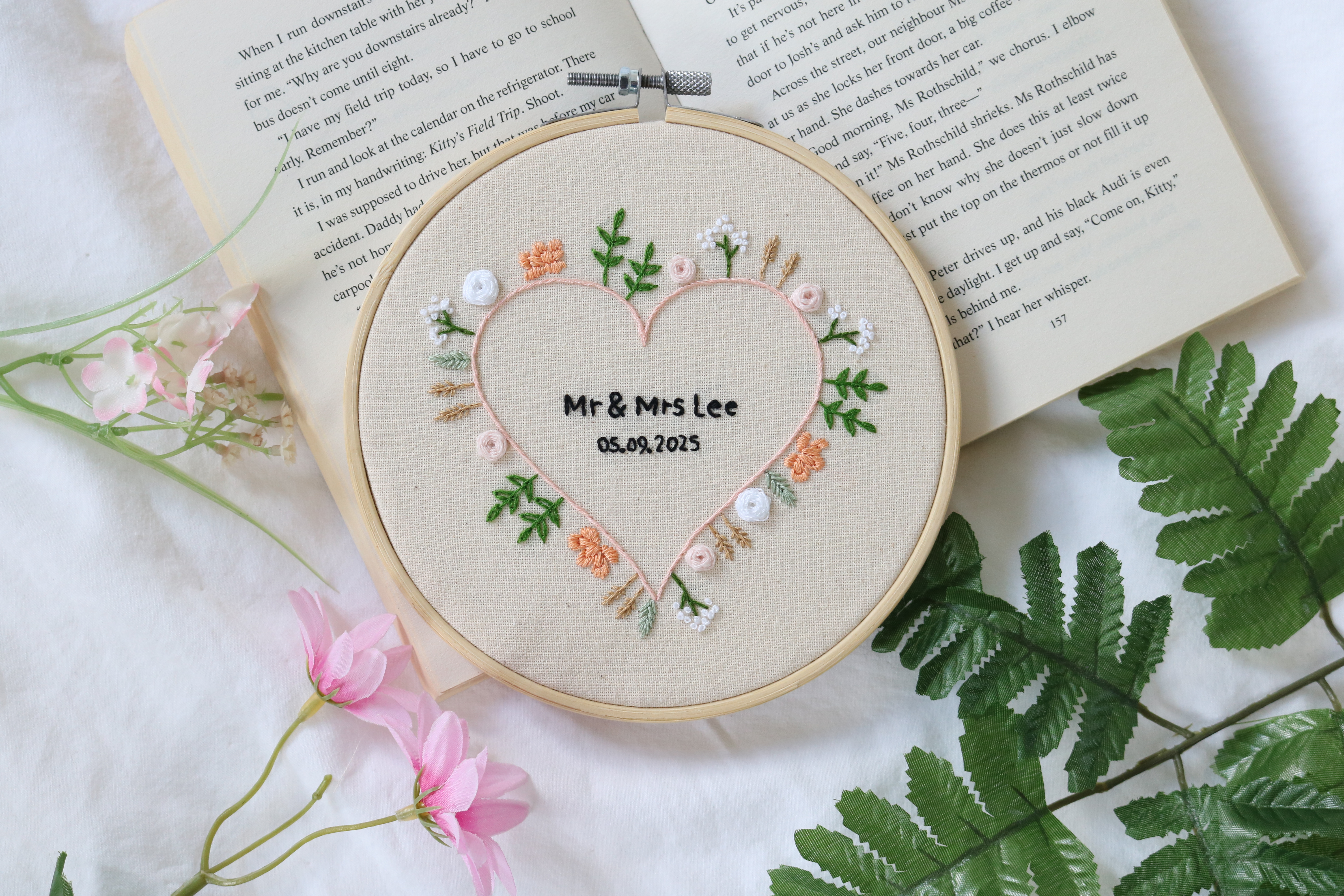 A 6 inch embroidery hoop hand embroidered with wedding flowers in a heart shape and the name 'Mr and Mrs Lee' embroidered in the middle