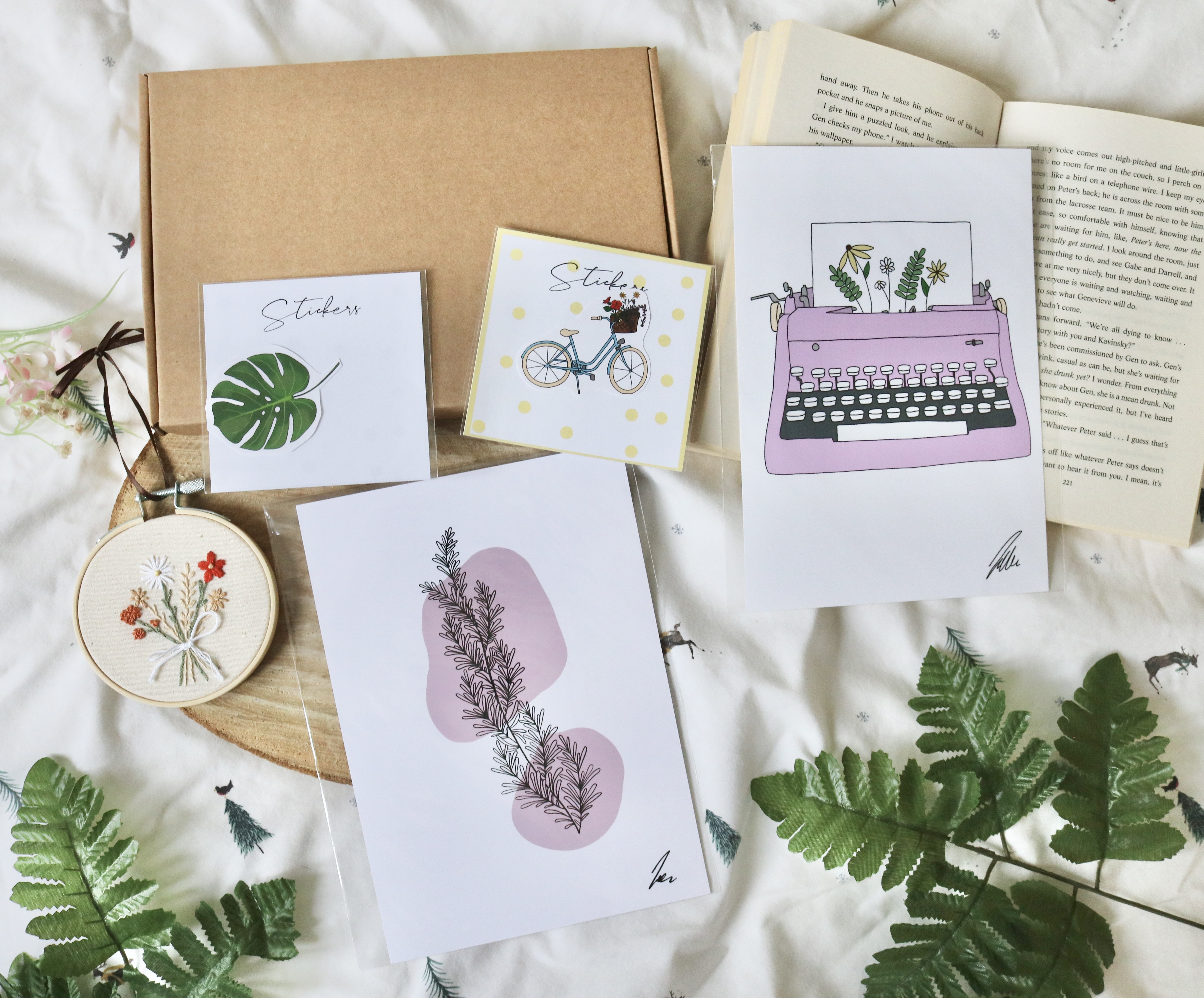 A photo of a small mystery box which includes a 3 inch hand embroidered decor hoop, 2 prints, and 2 stickers