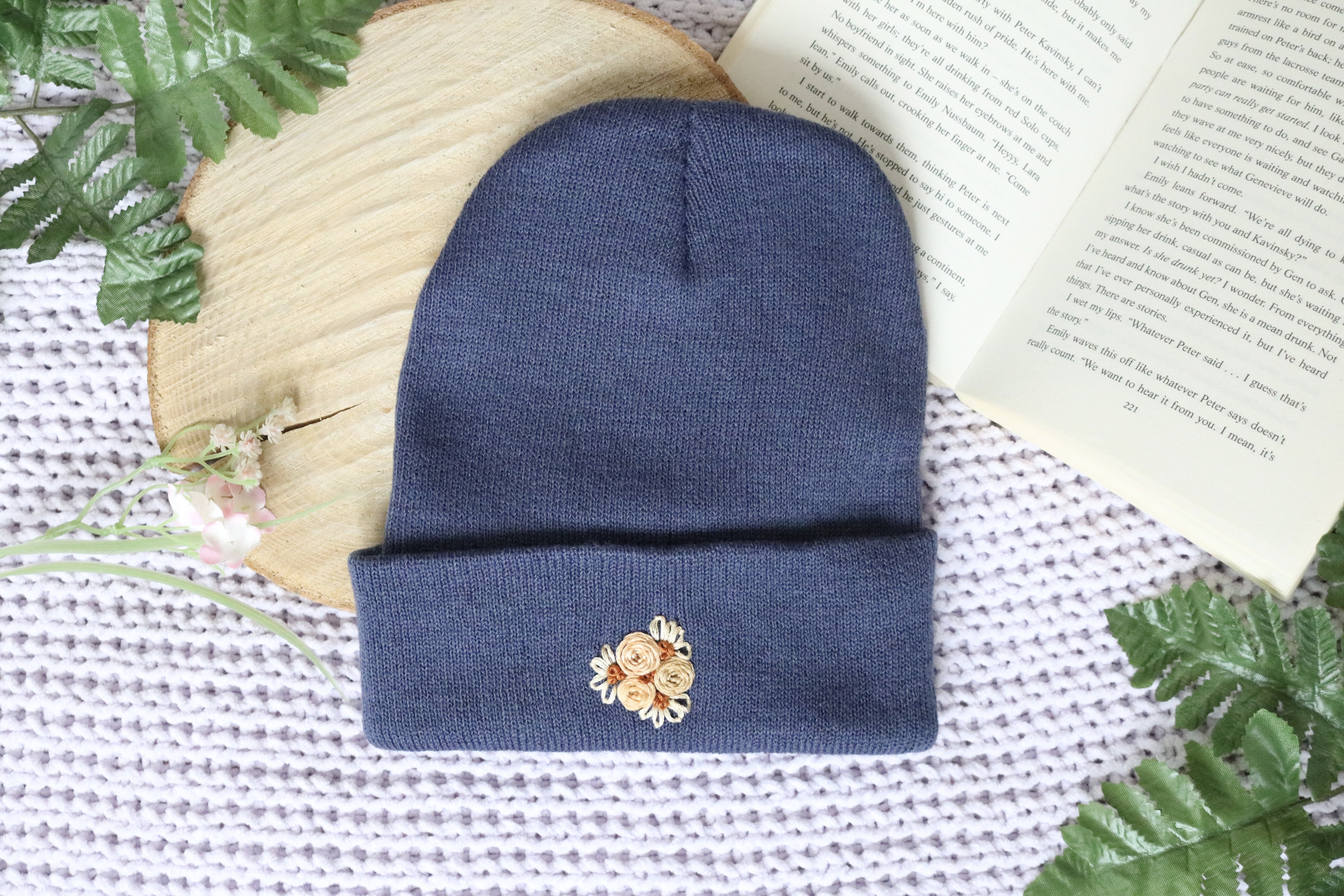 A dark jean blue beanie hand embroidered with three golden roses and 3 golden daisies