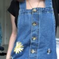 A blue denim pinafore dress hand embroidered with a yellow flower and bee