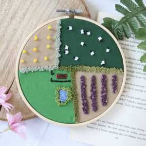 A 6 inch hoop hand embroidered with an aerial view of the countryside and fields. Featuring hay bales, sheep, lavender, a barn, and a pond.