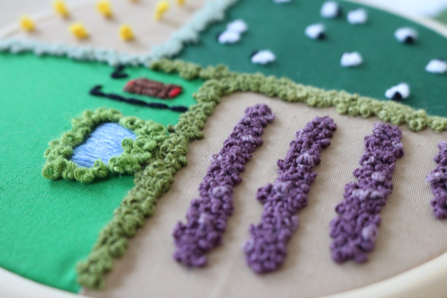 A hand embroidered lavender field with a pond and barn in the next field over