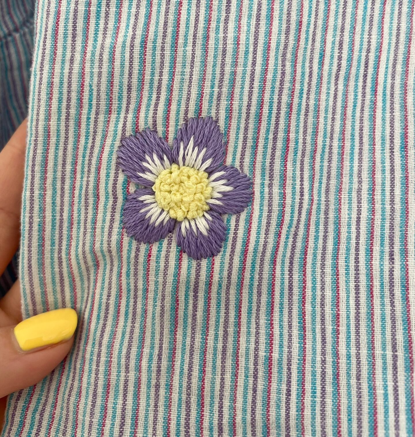 A purple and yellow flower hand embroidered over a hole in a t-shirt