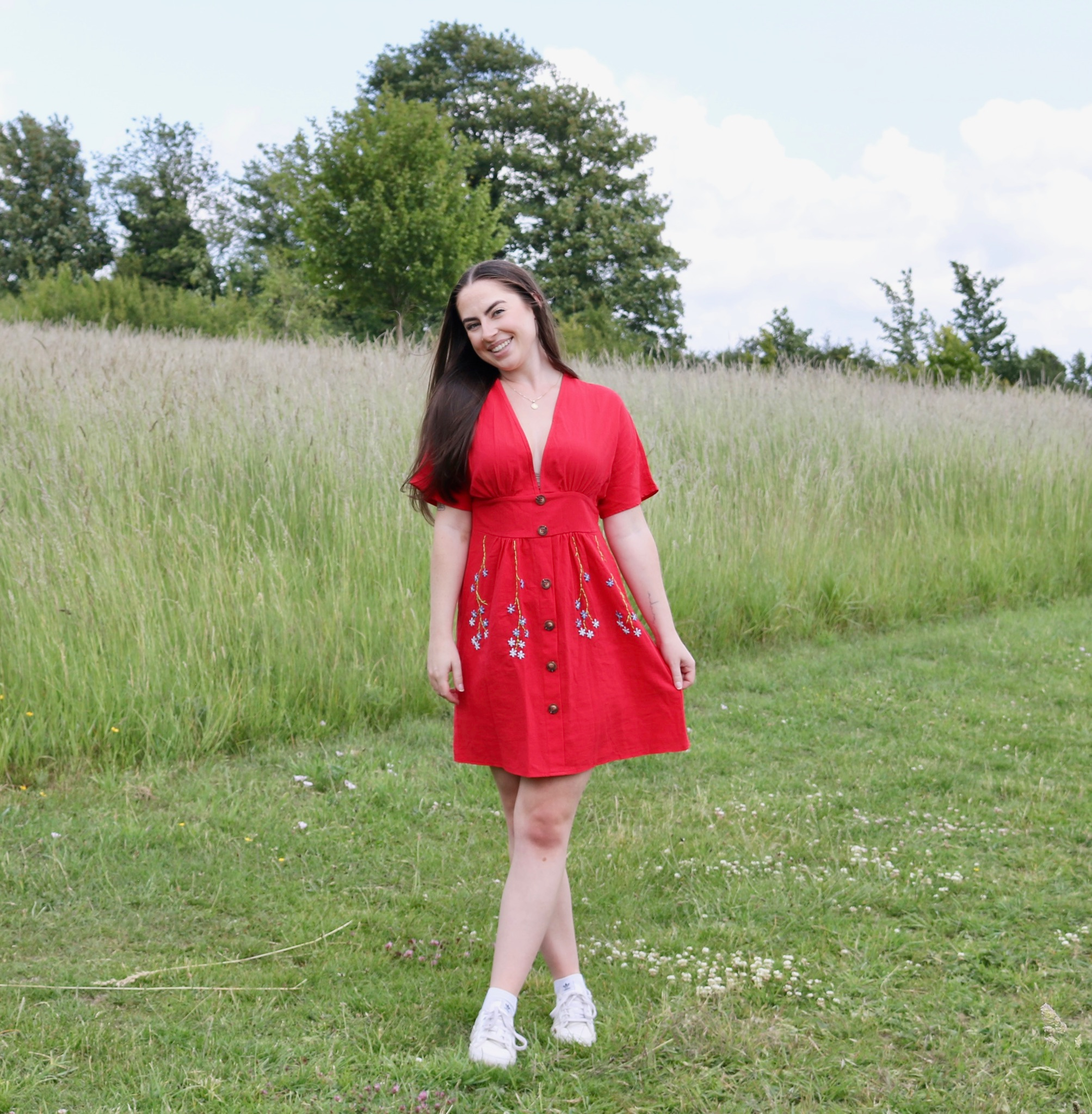 A brunette girl wearing a red button up dress hand embroidered with blue forget me not flower vines on the skirt