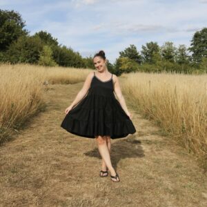 A brunette girl wearing a black floaty dress hand embroidered with a white zigzag trim at the neckline