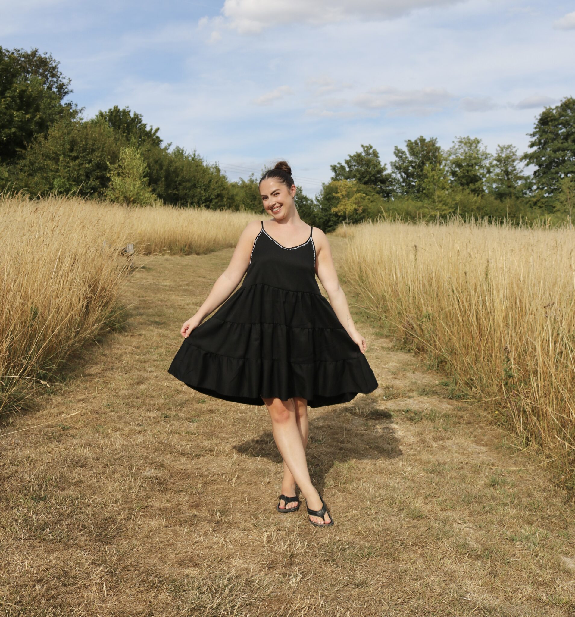 A brunette girl wearing a black floaty dress hand embroidered with a white zigzag trim at the neckline