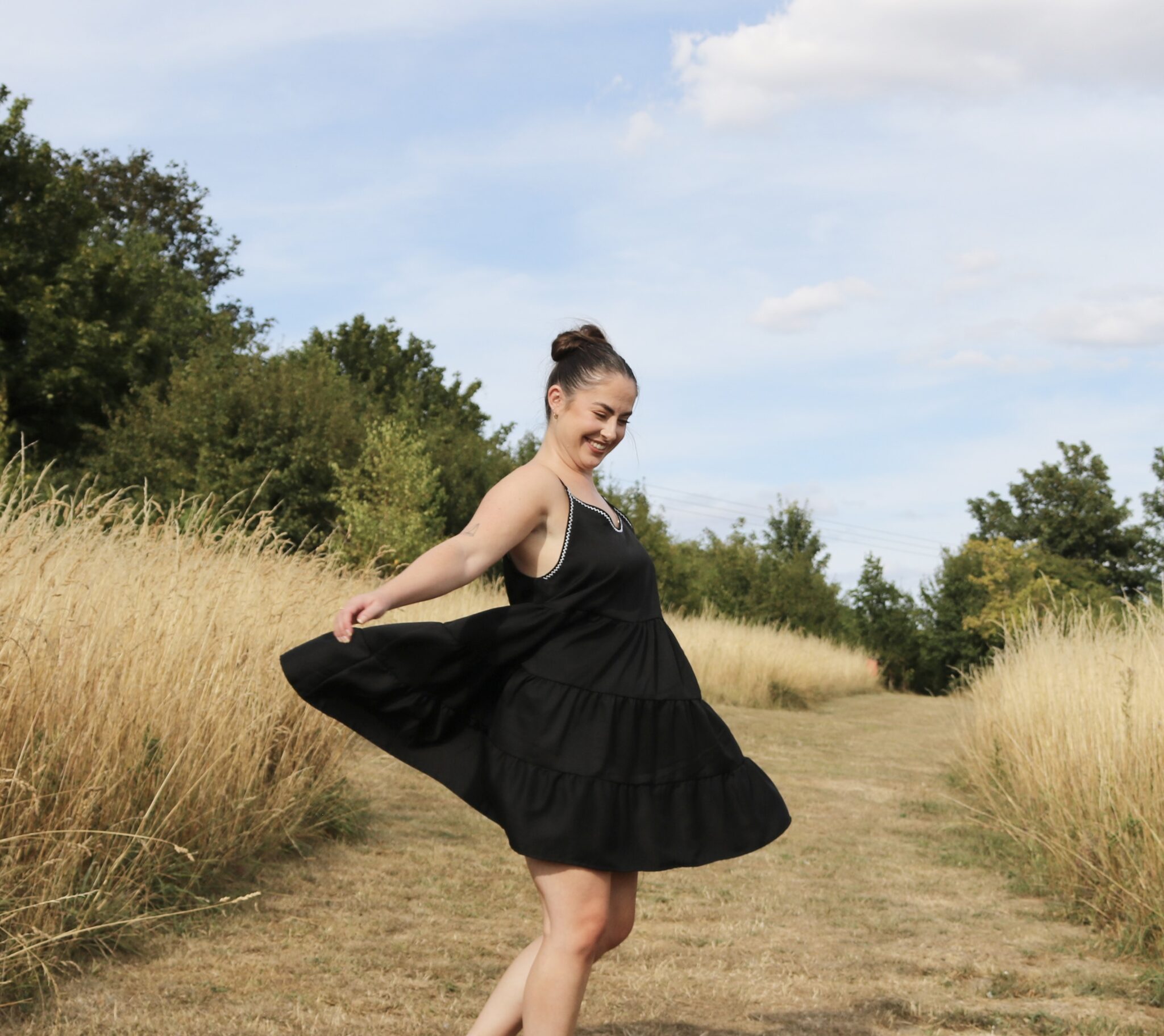 A brunette girl wearing a black swing dress twirling in a field